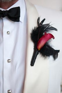 a man wearing a white tuxedo with black feathers and a red flower in his lapel