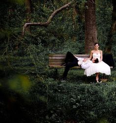 a bride and groom sitting on a park bench in the dark forest with their feet propped up against each other