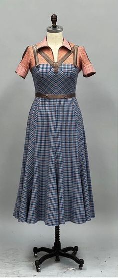 a dress on a mannequin with an orange top and blue plaid skirt, in front of a gray background