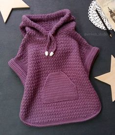 a purple crocheted dog sweater next to a white star on a black surface