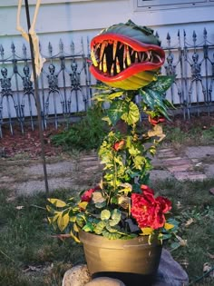 a flower pot with a fake dinosaur's mouth sticking out from it, sitting on a rock in front of a house