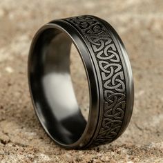 a black ring with an intricate design on it's center is sitting in the sand