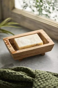 a soap bar sitting on top of a wooden tray next to a green blanket and window