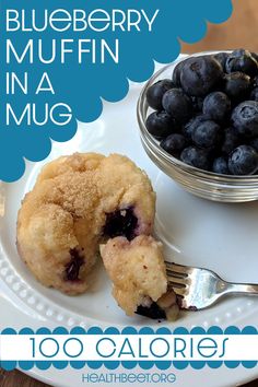 blueberry muffin in a mug on a plate with a fork and bowl of berries