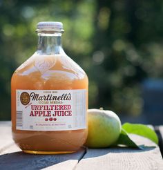 a bottle of unfittered apple juice next to an apple on a table