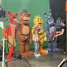 children standing in front of five cartoon characters on stage with microphones and sound equipment