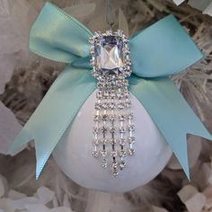 a white ornament with a light blue bow and diamond brooch hanging from it's side