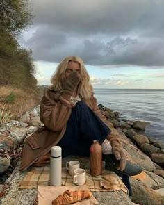 a woman is sitting on the rocks by the water with her hands in her mouth