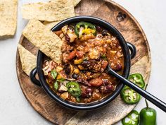 a bowl filled with chili and tortilla chips on top of a wooden plate