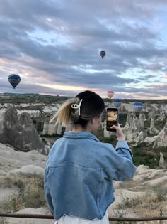 a woman taking a photo of hot air balloons in the sky