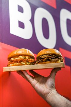 a hand holding a tray with two sandwiches on it and the word boo spelled in large letters