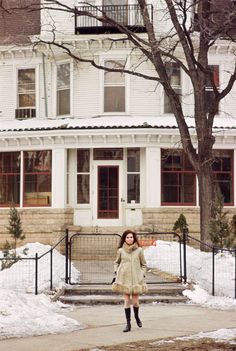 a woman standing in front of a white house with snow on the ground and trees