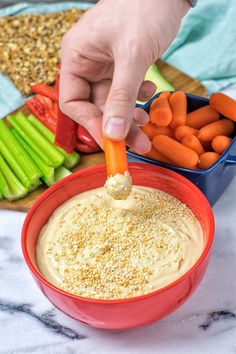 a person dipping carrots into a bowl of dip