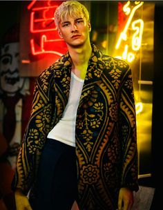 a male model with blonde hair wearing a black and gold jacket, white shirt and black pants