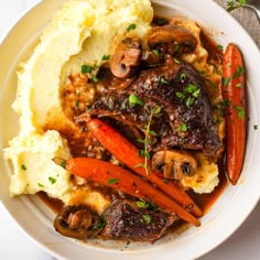 a white plate topped with mashed potatoes, carrots and meat covered in gravy