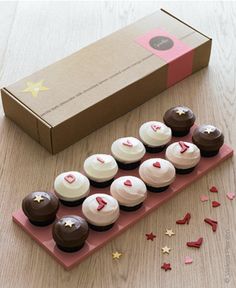 cupcakes with white and chocolate frosting are arranged on a pink tray next to a cardboard box