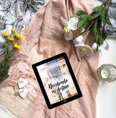 a tablet sitting on top of a pink blanket next to flowers and other items in front of it