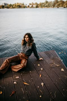 a woman is sitting on a dock by the water