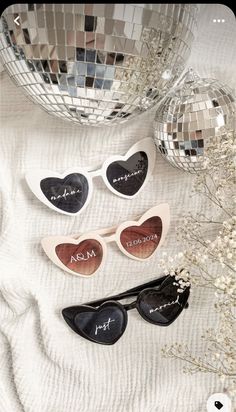 three heart shaped sunglasses sitting on top of a white blanket next to a disco ball