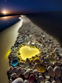 a heart made out of sea glass sitting on the beach next to the ocean at night