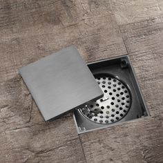 a square metal box with a hole in the middle on a wooden floor that has holes and grates