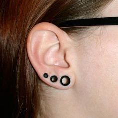 a woman with black ink on her ear has three small circles attached to the side of her ear