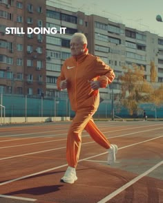 an old man is running on a tennis court with buildings in the background and words still doing it