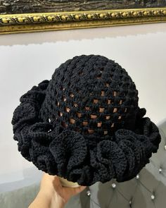 a person holding up a black crocheted hat in front of a painting on the wall