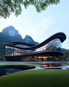 the building has curved glass walls and is surrounded by green grass, with mountains in the background