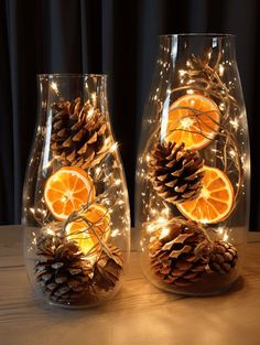 two clear glass vases with orange slices and pine cones on the sides, decorated with lights