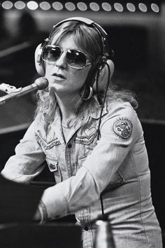 a woman wearing headphones and holding a microphone in front of her face while standing next to a piano