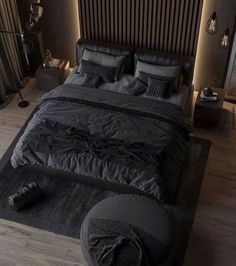 a large bed with black sheets and pillows in a dark colored room, surrounded by wooden flooring