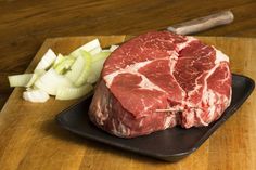 a piece of meat sitting on top of a cutting board next to onions and a knife