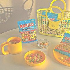 a yellow basket filled with lots of candy next to two small bowls and some cups