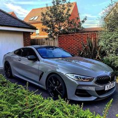 a silver bmw car parked in front of a house next to some bushes and trees