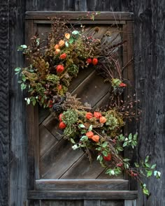 a wreath is hanging on the side of an old wooden door with autumn foliage and berries