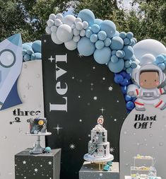 an astronaut themed birthday party with balloons, cake and desserts on pedestals in front of a backdrop