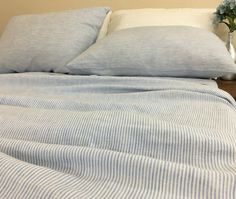 a bed with blue and white striped sheets, pillows and a vase filled with flowers