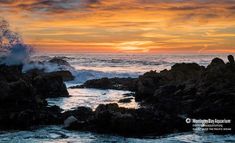 the sun is setting over the ocean with waves crashing on rocks in front of it