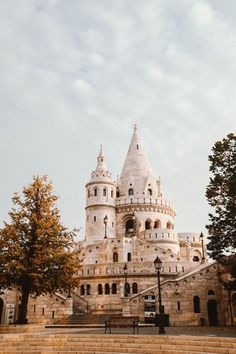 a large white castle sitting on top of a lush green field next to trees and stairs