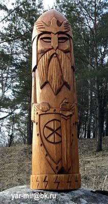 a carved wooden statue sitting on top of a rock in front of some pine trees