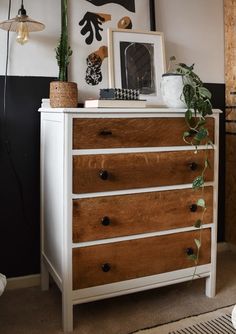 a white dresser with wooden drawers and plants on top