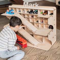 a young boy playing with toys on the floor in front of a wooden shelf that says mark