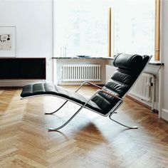 a black leather chaise lounge chair sitting on top of a hard wood floor next to a window