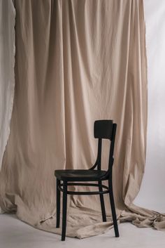 a black chair sitting in front of a beige backdrop with a drape on it