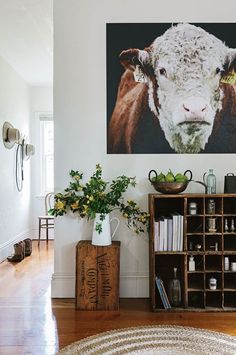 a living room with a cow painting on the wall next to a book shelf and bookshelf