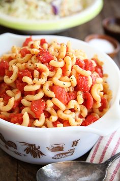 a white bowl filled with pasta and sauce on top of a table next to a fork