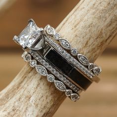 two wedding rings with black and white stones on them sitting on top of a tree branch