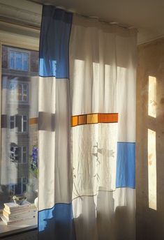 the sun is shining through some curtains in front of a window with books on it