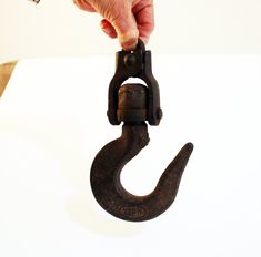 a hand holding an old metal hook on a white surface